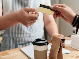 Kund räcker över medlemskort till kassapersonal. En kaffe och en papperspåse står på kassadisken.